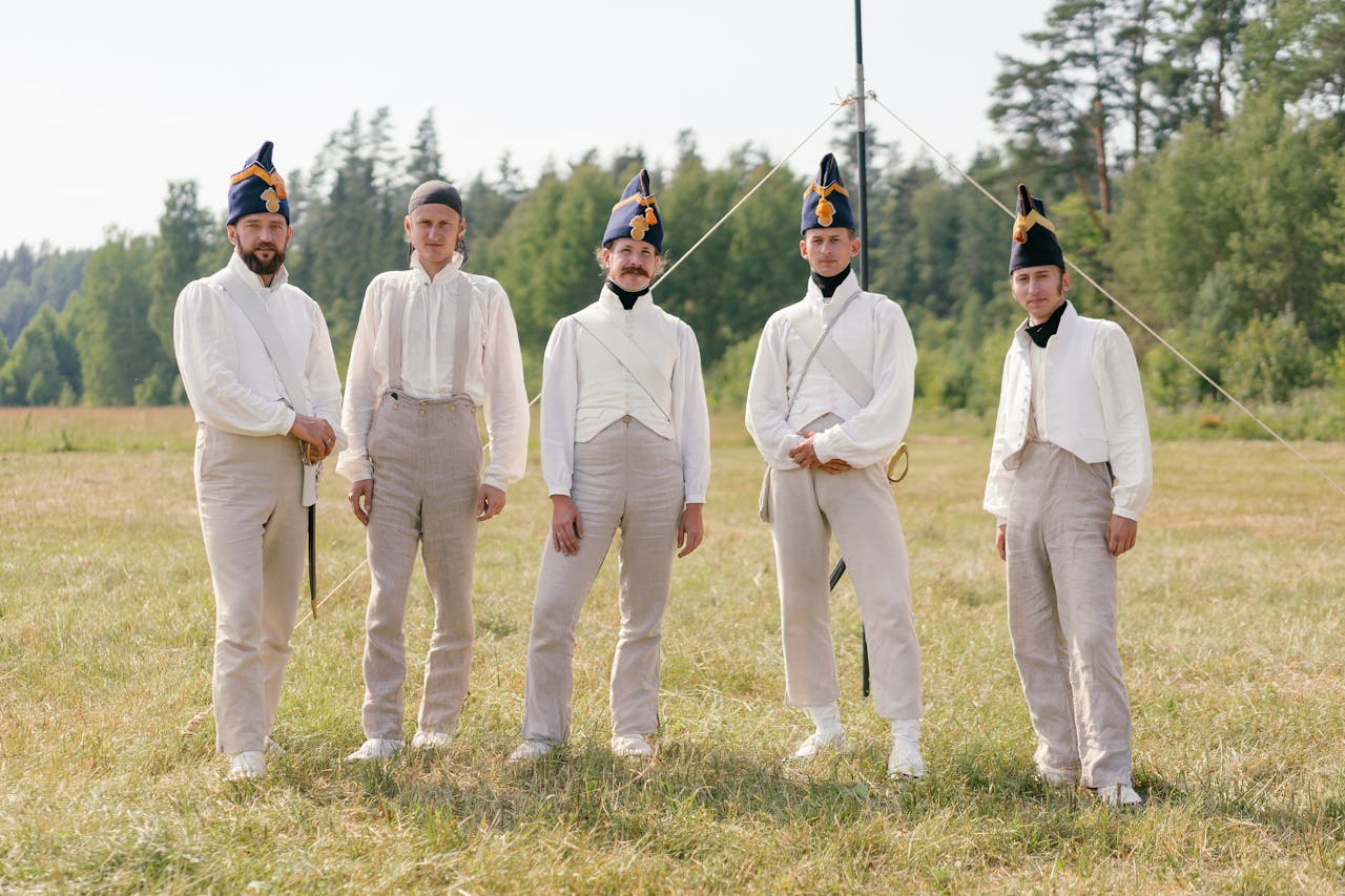 Five men in historical military uniforms stand outdoors during a reenactment event.